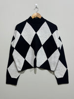 Black and white oversized diamond-pattern knitted blouse with a high neckline, dropped shoulders and long sleeves.