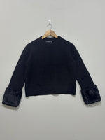Black crew-neck pullover with a boxy silhouette, long sleeves and wide fluffy cuffs on a wooden hanger.