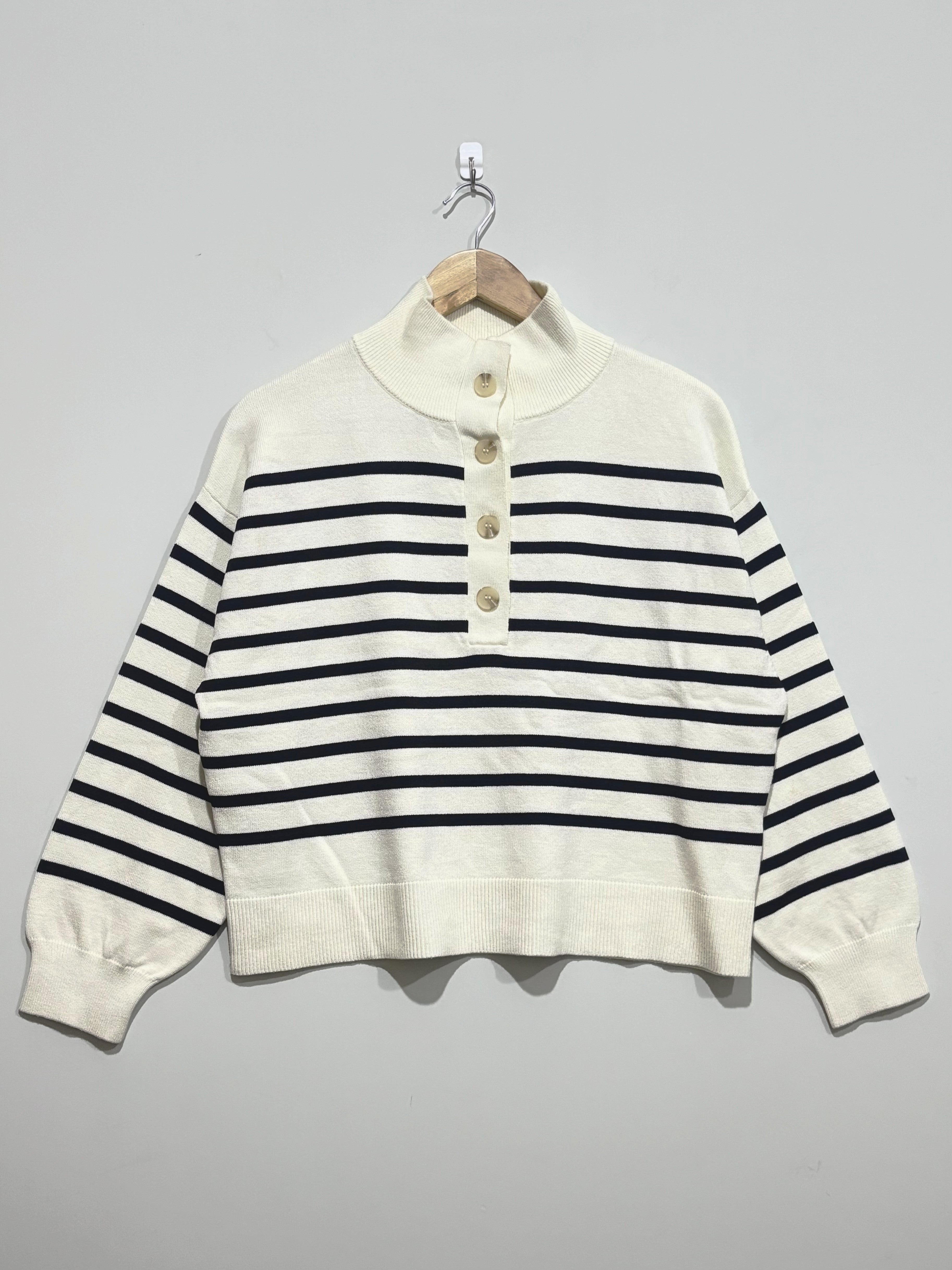 Cream knitted pullover with black horizontal stripes, a high button neckline, dropped shoulders, full long sleeves and ribbed cuffs and hem.