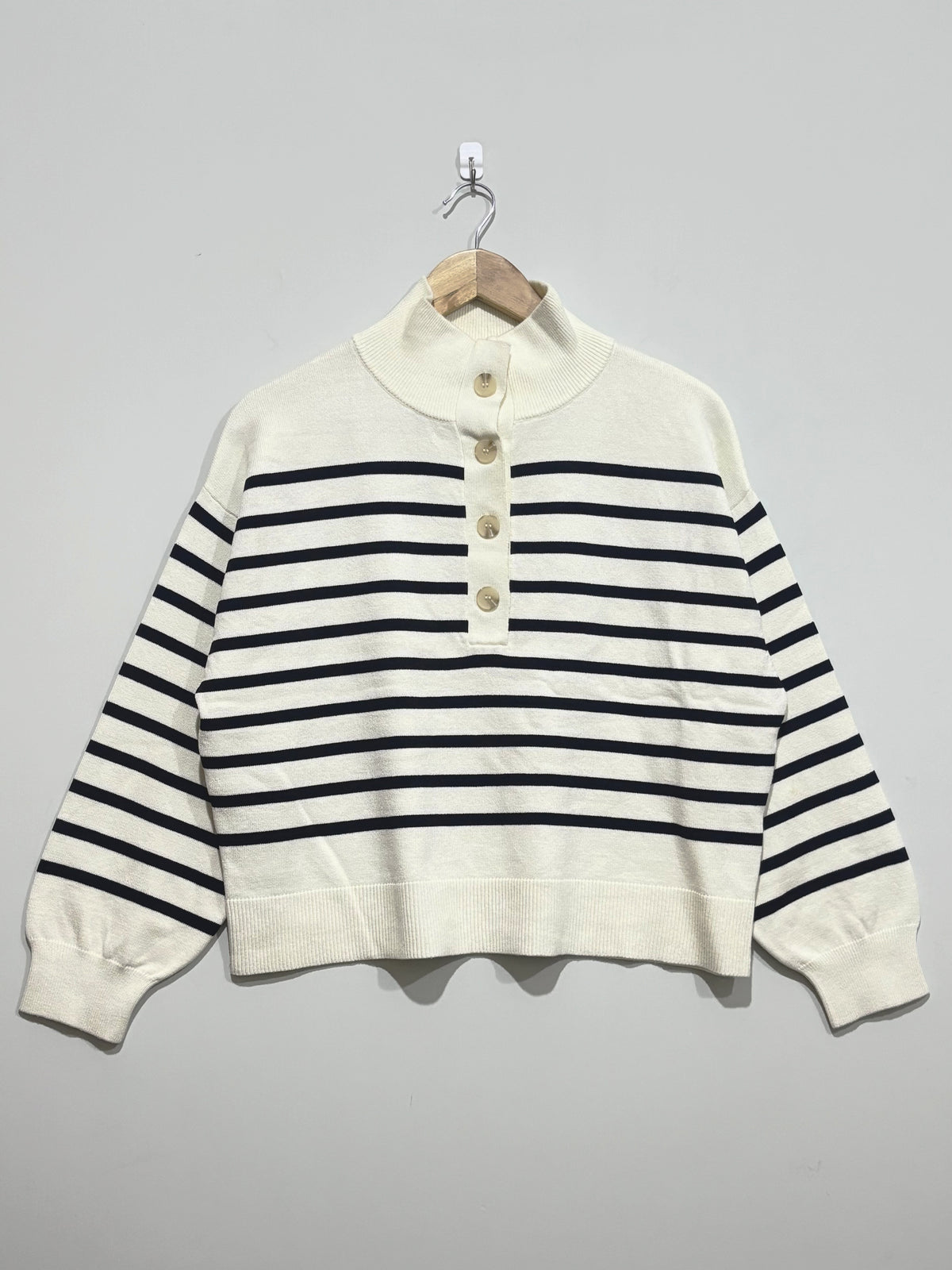 Cream knitted pullover with black horizontal stripes, a high button neckline, dropped shoulders, full long sleeves and ribbed cuffs and hem.