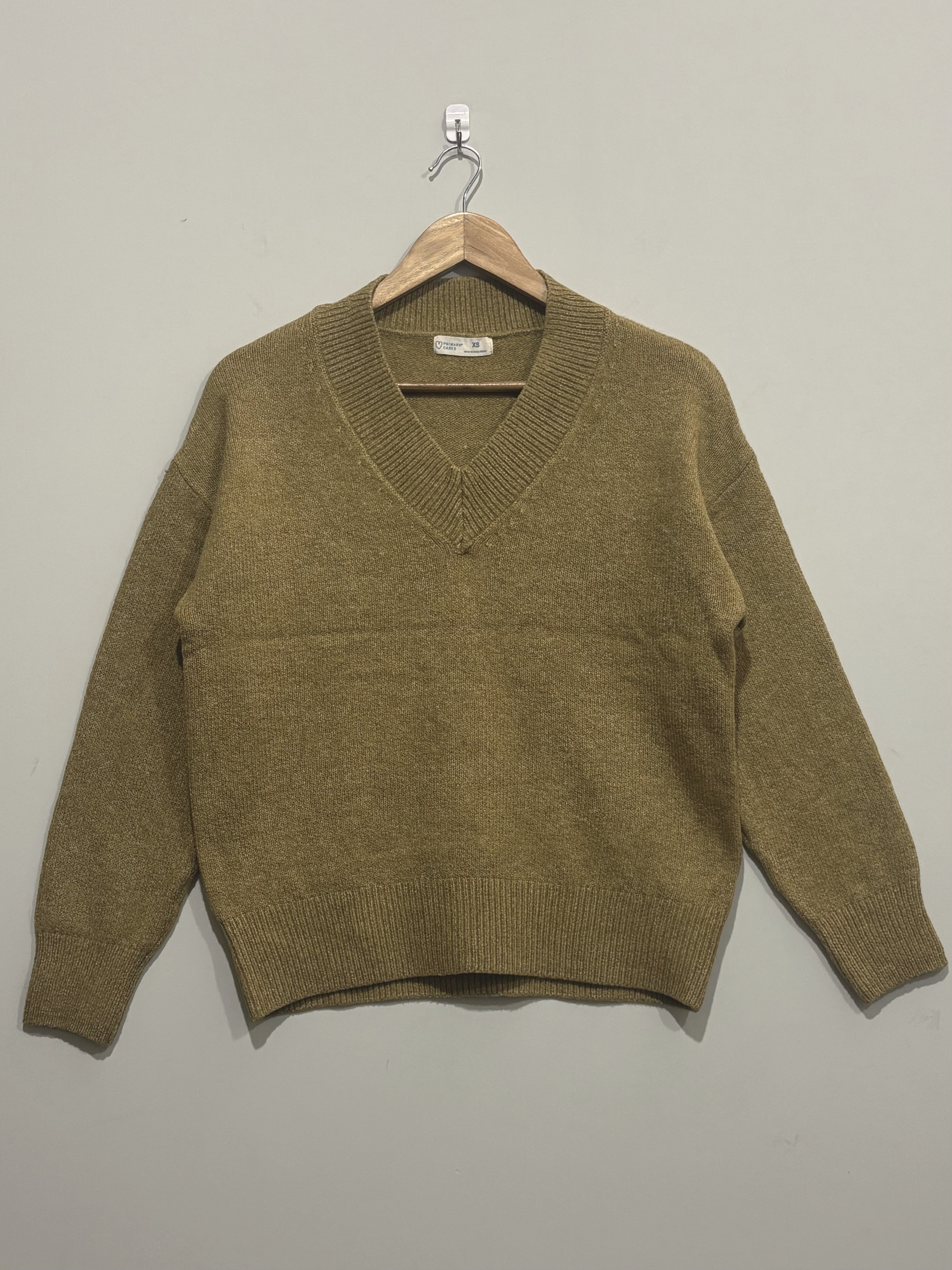 Olive green knitted V-neck pullover with dropped shoulders, long sleeves and wide ribbed cuffs and hem on a wooden hanger.