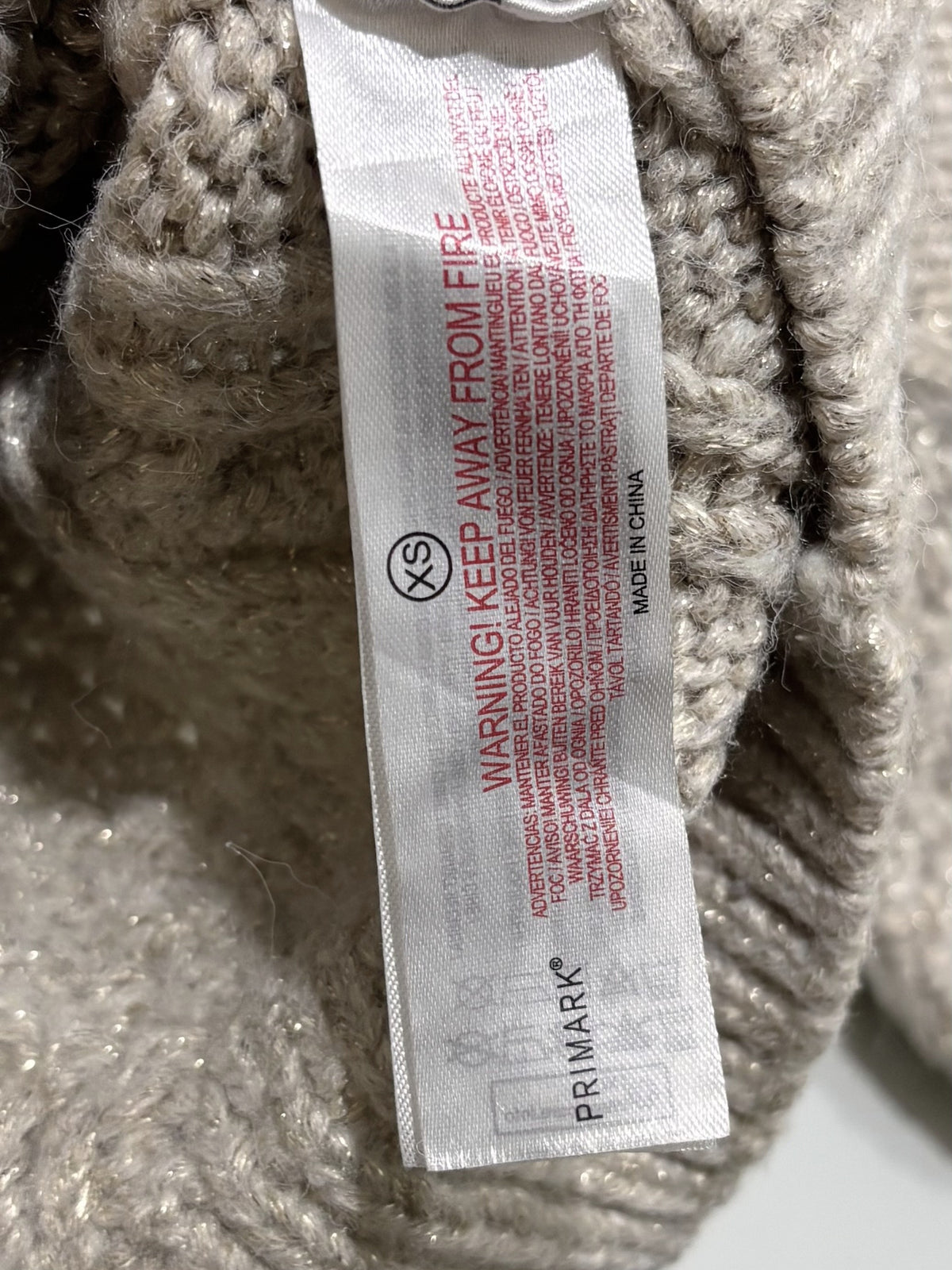 Beige crew-neck pullover with diamond cable-knit patterns, dropped shoulders, long sleeves and ribbed trims on a wooden hanger.