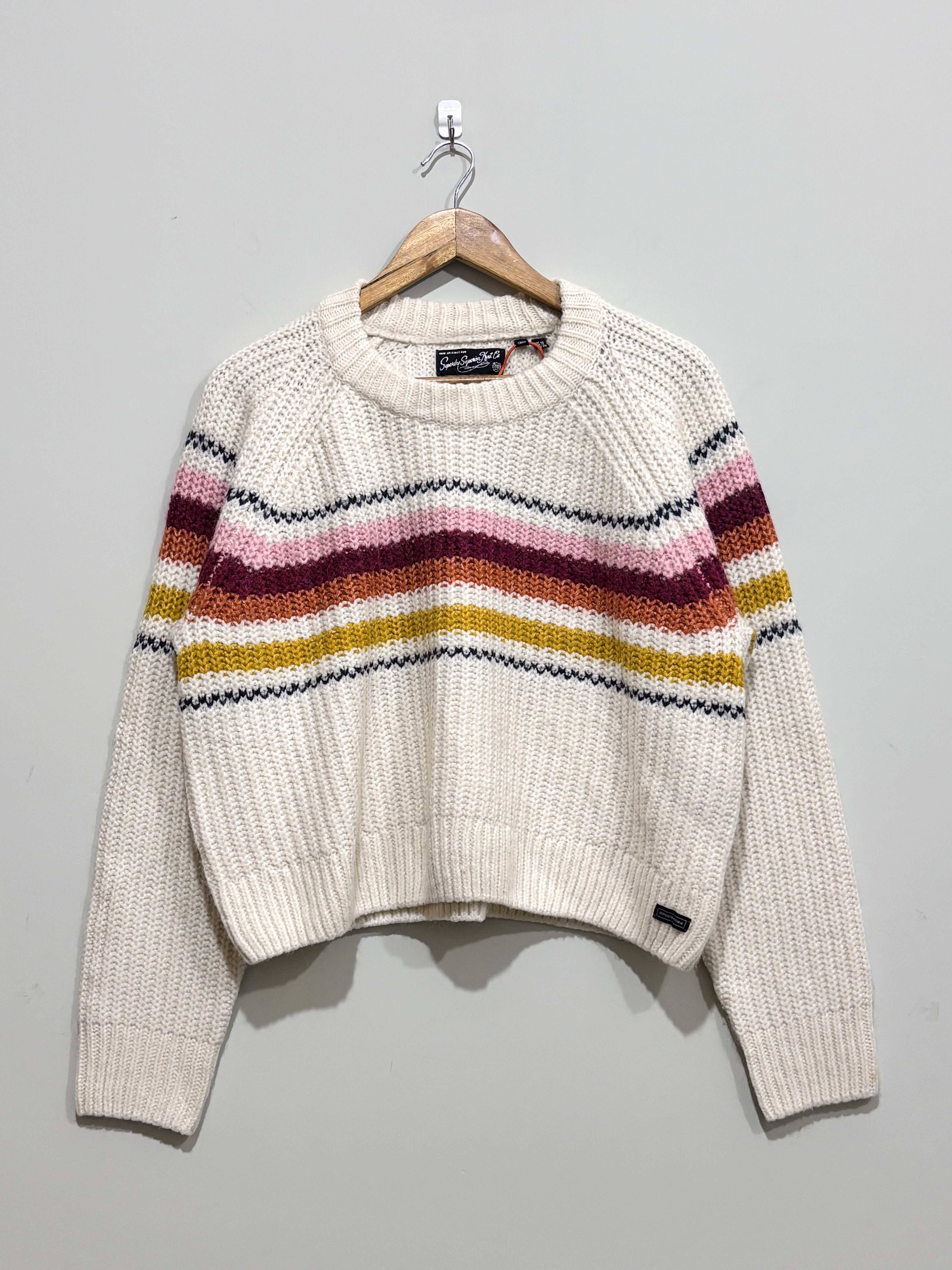 Cream textured knit pullover with pink, burgundy, orange, mustard and dark horizontal stripes across the chest and sleeves, a crew neck and ribbed trims.