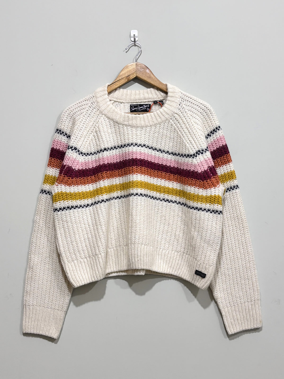 Cream textured knit pullover with pink, burgundy, orange, mustard and dark horizontal stripes across the chest and sleeves, a crew neck and ribbed trims.