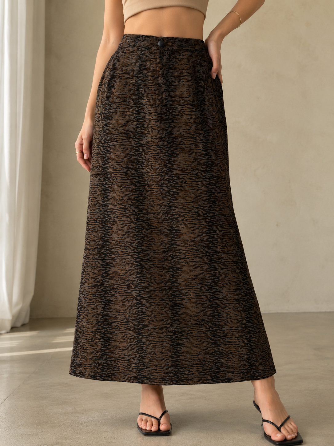 Person wearing a long brown patterned skirt in a neutral setting