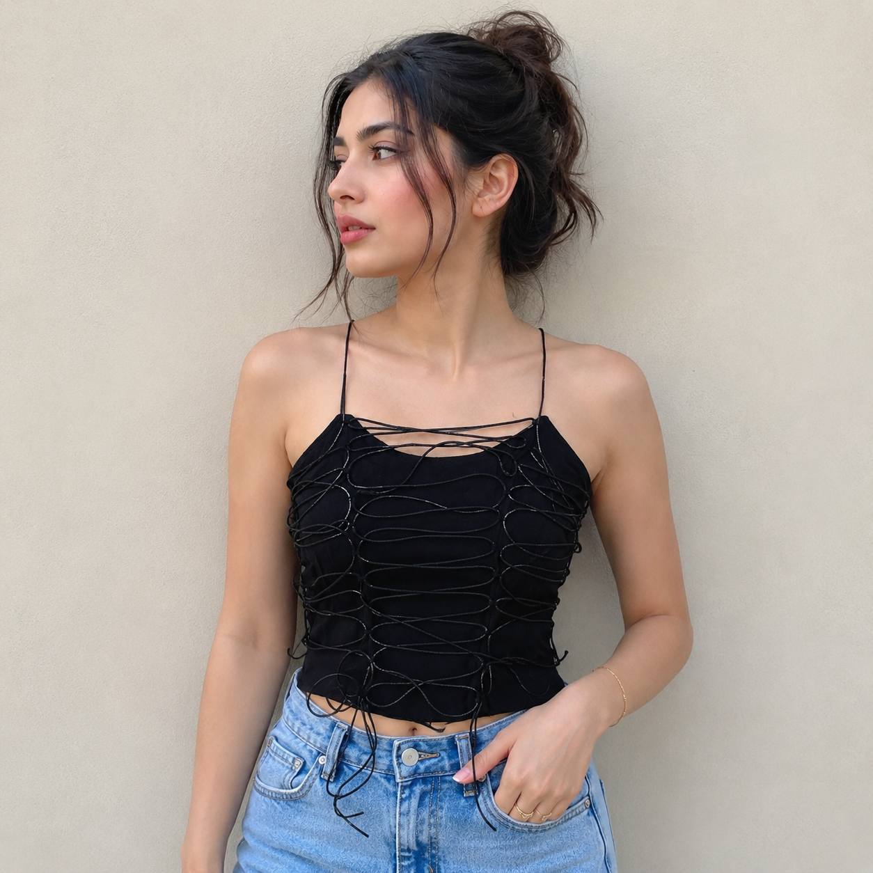 Woman wearing a black strappy top and blue jeans against a beige wall