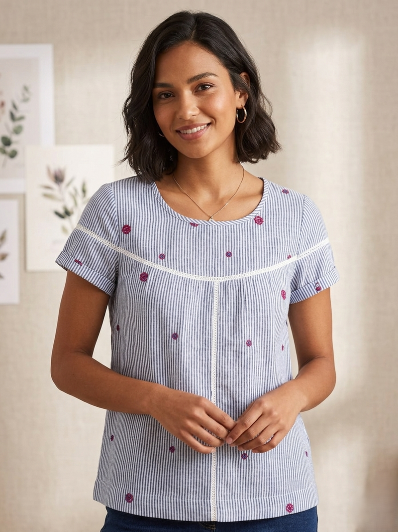 Woman wearing a blue and white striped shirt with red polka dots in a neutral setting