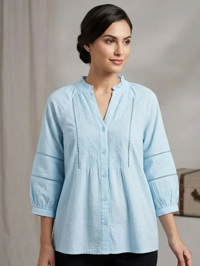 Woman wearing a light blue blouse with intricate detailing on a neutral background