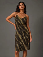 A woman modeling a sleeveless spaghetti-strap midi dress with a black and gold abstract spotted pattern, posed against a solid dark gray studio background.