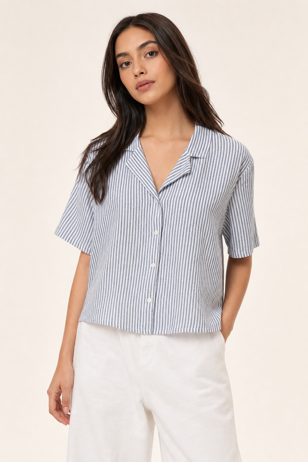 Woman wearing a blue and white striped shirt with white pants on a beige background