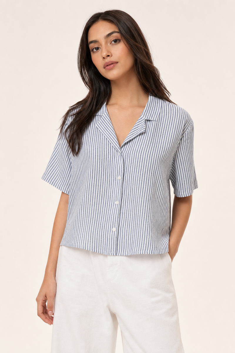 Woman wearing a blue and white striped shirt with white pants on a beige background