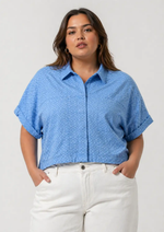 Woman wearing a blue patterned shirt and white pants on a plain background