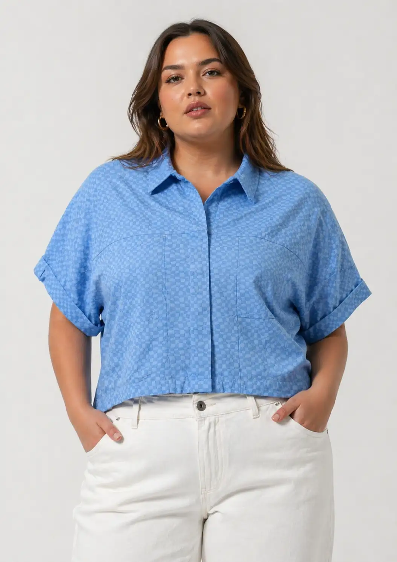 Woman wearing a blue patterned shirt and white pants on a plain background