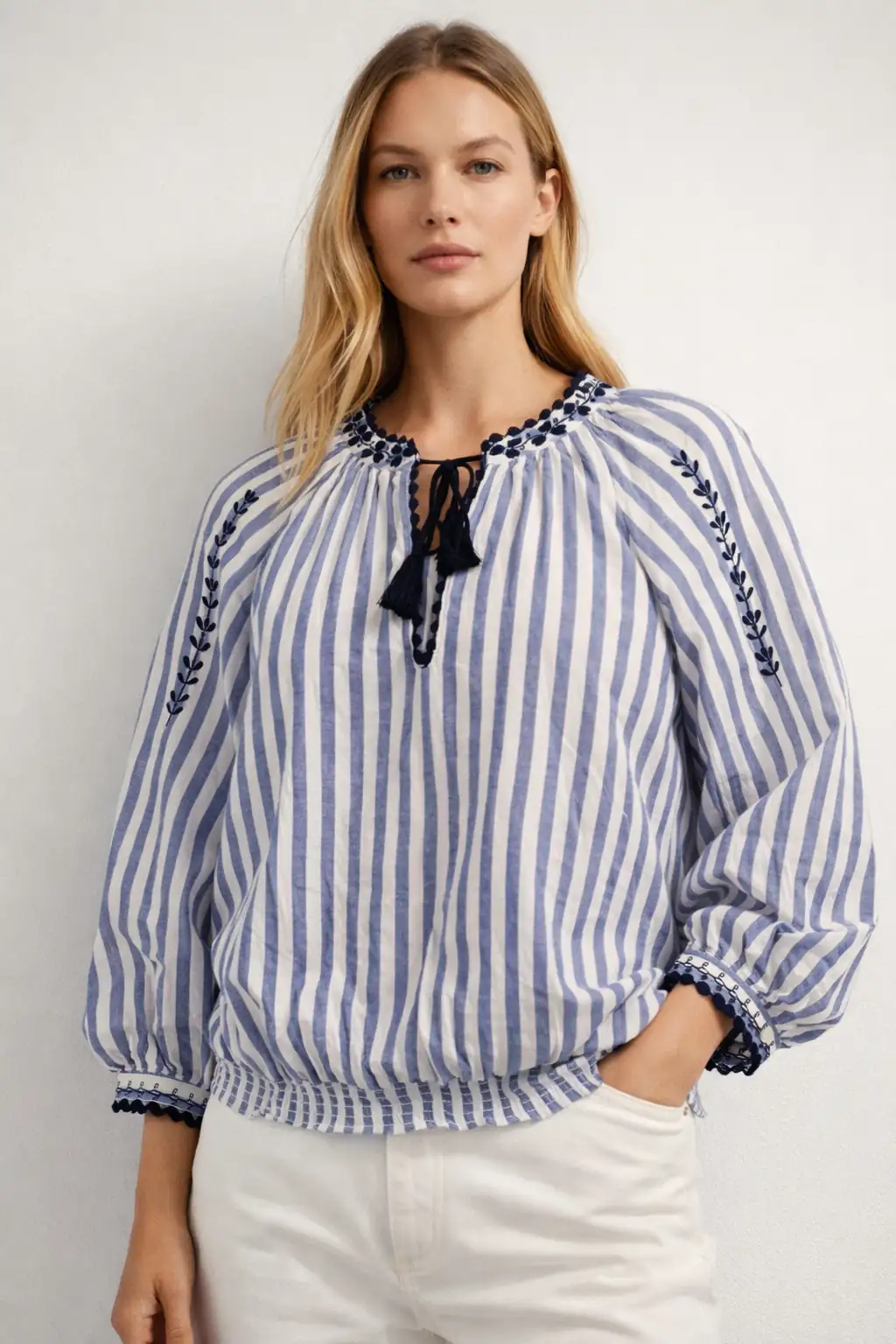 Woman wearing a blue and white striped blouse with embroidery on a plain background