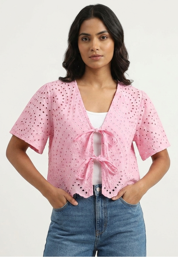 Woman wearing a pink blouse with a bow detail and blue jeans on a white background