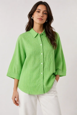 Woman wearing a bright green button-up shirt and white pants on a plain background
