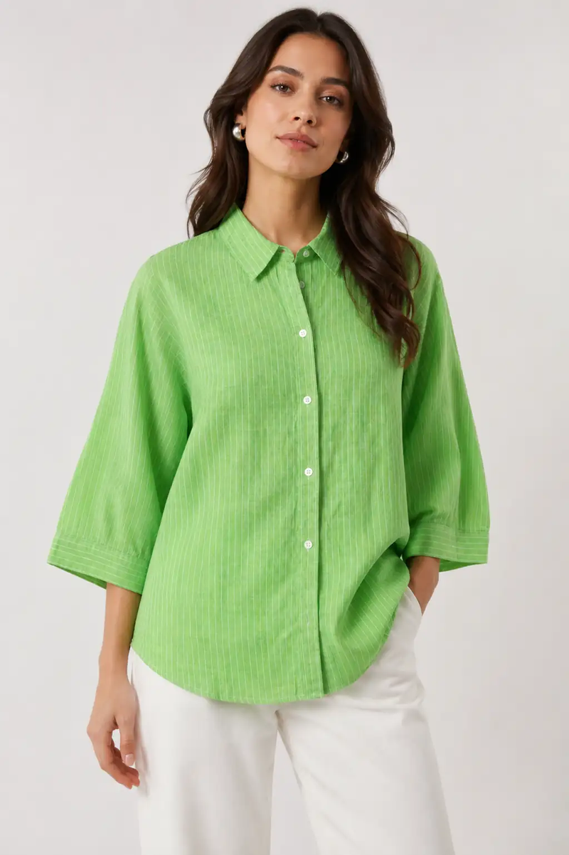 Woman wearing a bright green button-up shirt and white pants on a plain background