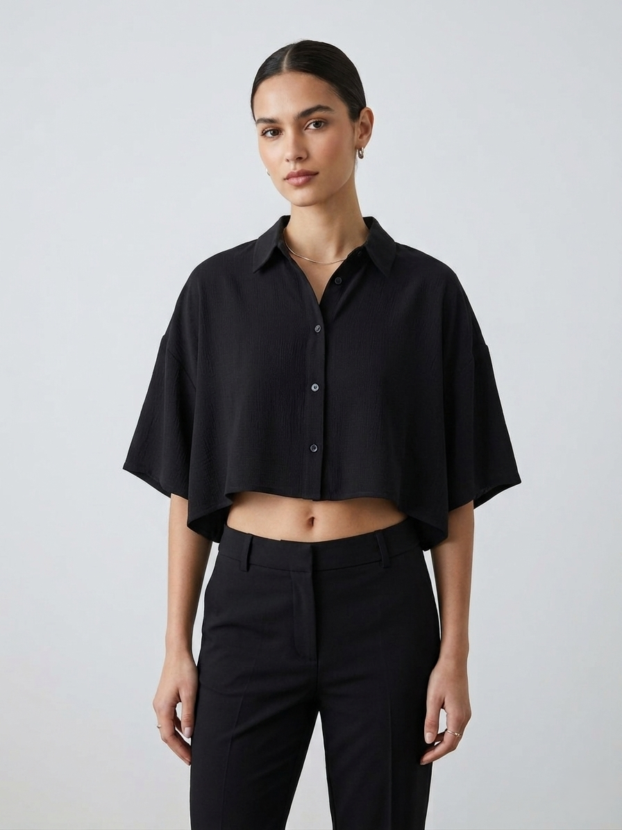 Woman wearing a black cropped shirt and black pants against a light gray background