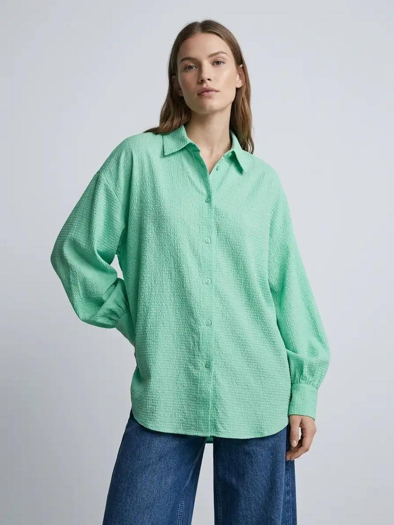 Woman wearing a green shirt and blue jeans on a plain background